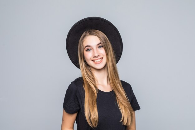 Increíble joven con cabello dorado vestida de negro con sombrero retro sonríe aislado sobre fondo