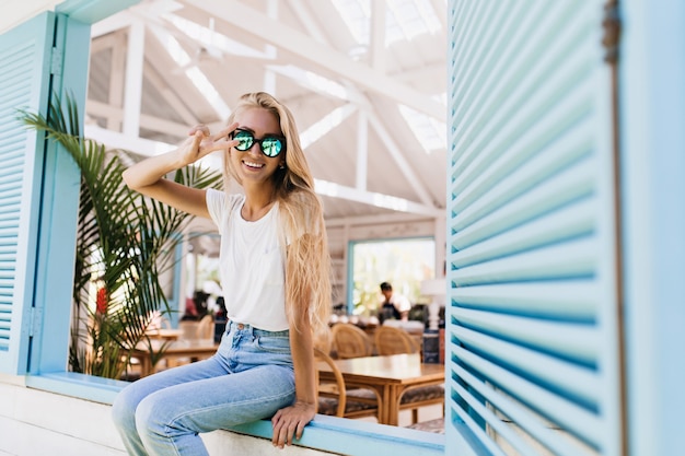 Foto gratuita increíble modelo femenino europeo en camiseta blanca posando con gafas de sol brillantes y jeans azules.