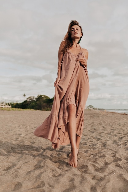 Increíble modelo de mujer con cabello largo con un vestido largo en la playa a la luz del sol junto al mar