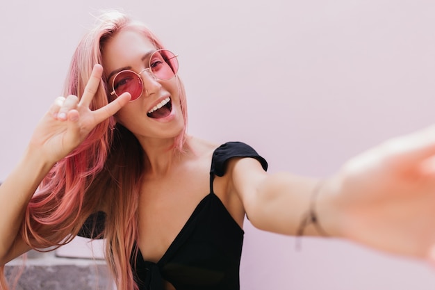 Increíble mujer bronceada en vestido negro posando en estudio con sonrisa.