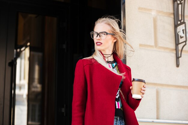 Increíble mujer caucásica joven caminando al aire libre tomando café.