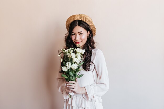 Increíble mujer japonesa rizada con flores de eustoma. Disparo de estudio de tímida mujer asiática con ramo.