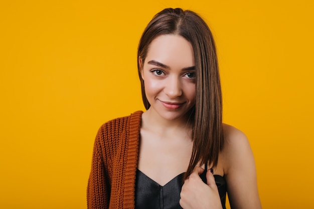 Increíble mujer joven con cabello lacio castaño sonriendo juguetonamente. Atractiva chica europea con grandes ojos oscuros posando.