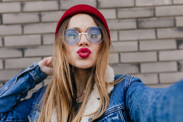 Increíble mujer joven con maquillaje brillante posando con expresión de la cara de besos. Toma de primer plano de una chica rubia de ensueño jugando mientras se toma una foto de sí misma.