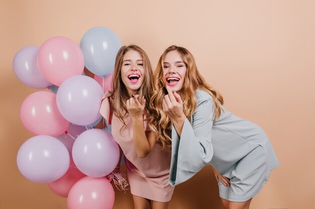 Increíble mujer joven rizada en vestido azul posando junto a la hermana en su cumpleaños