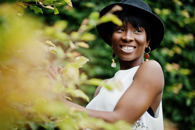 Increíble mujer modelo afroamericana en pantalones verdes y sombrero negro posado en el parque