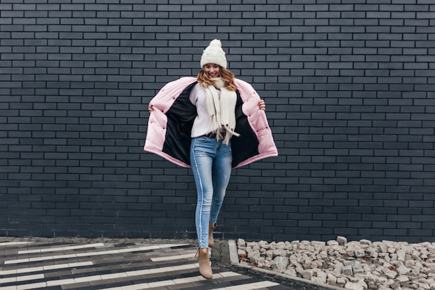 Foto gratuita increíble mujer en traje de invierno divertido bailando en la calle urbana. modelo femenino en jeans disfrutando de la sesión de fotos en un día frío.