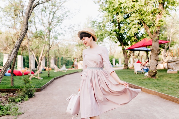 Increíble señorita jugando con su largo vestido morado claro, caminando en el callejón del parque antes de hacer un picnic con amigos