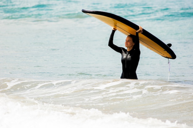 Foto gratuita increíble vista. hermosa niña se encuentra con una tabla de surf en la orilla del océano