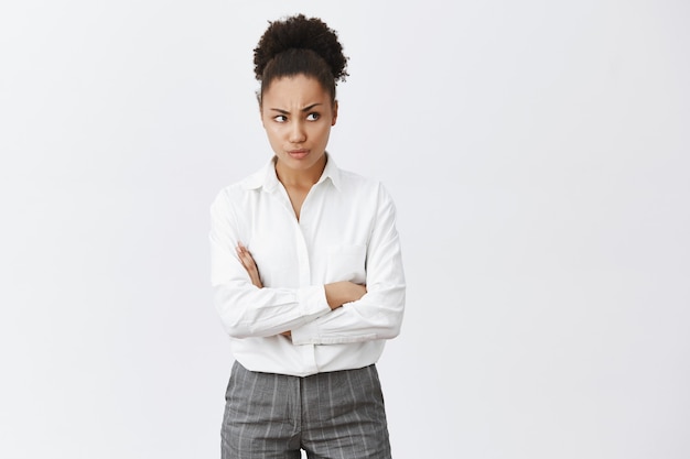 Indecisa mujer afroamericana con los brazos cruzados en el pecho y frunciendo el ceño, mirando a la derecha con expresión preocupada