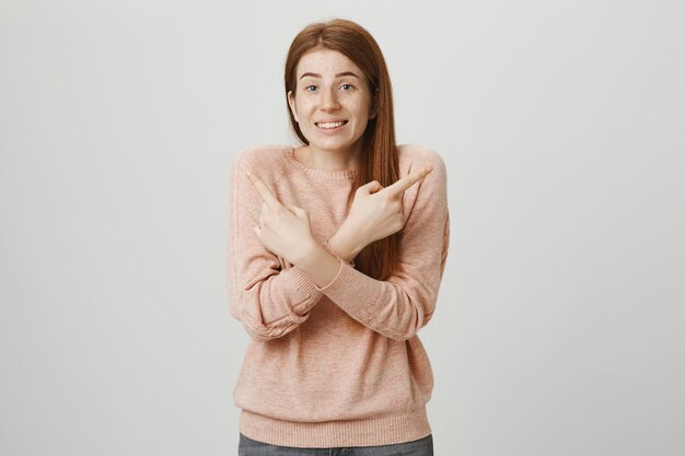 Indeciso linda chica pelirroja apuntando hacia los lados