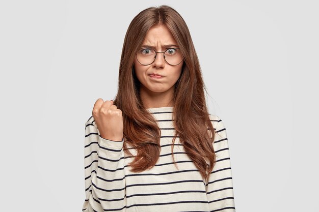 Indignado joven con gafas posando contra la pared blanca