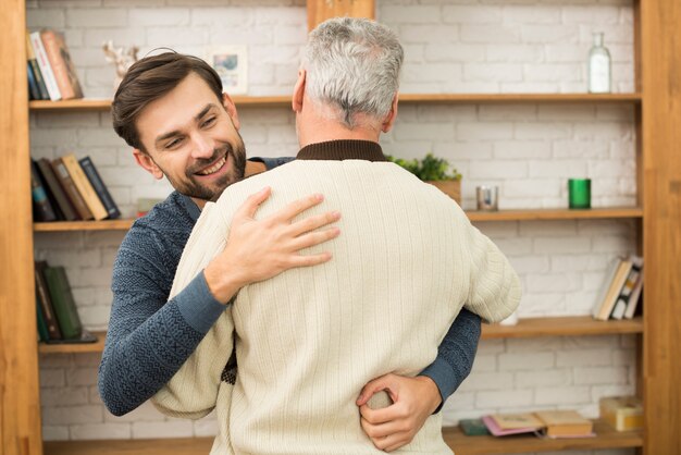 Individuo feliz joven que abraza con el hombre envejecido cerca de los estantes