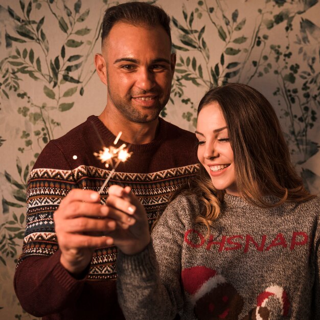 Individuo sonriente cerca de señora alegre con las luces de Bengala llameantes