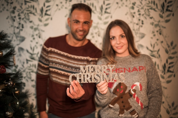 Individuo sonriente cerca de señora alegre con la tableta de la Feliz Navidad cerca del árbol de abeto adornado