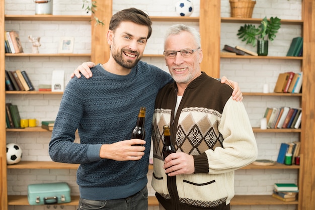 Individuo sonriente joven que abraza con el hombre feliz envejecido con las botellas