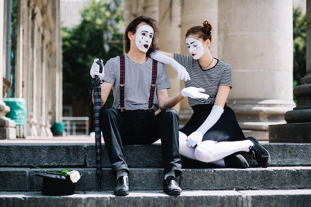 Infeliz artista de mimo masculino y femenino sentado en la escalera