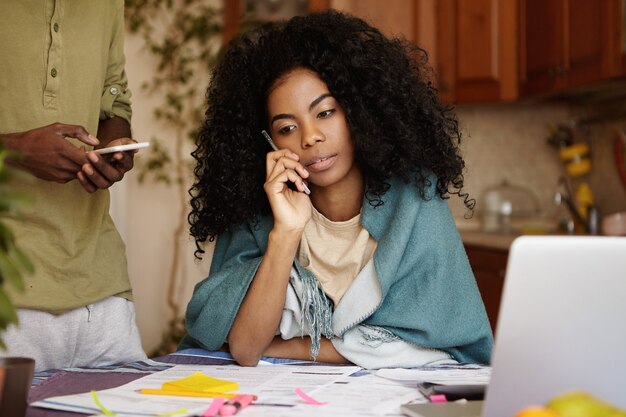 Infeliz y cansada mujer afroamericana con pelo rizado hablando por teléfono móvil