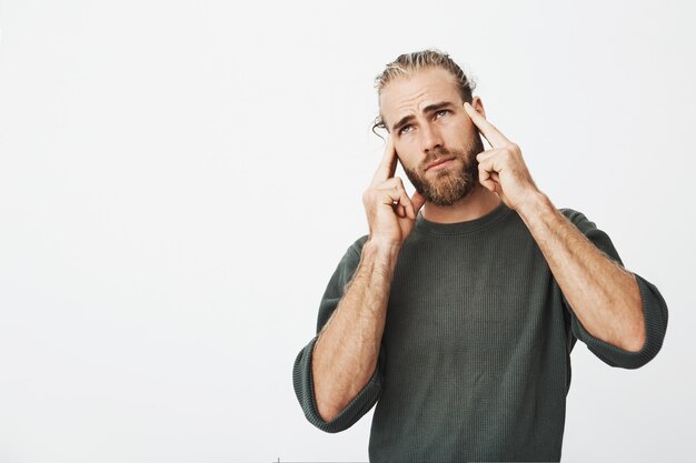 Infeliz hombre guapo con buen peinado y barba sintiéndose extremadamente cansado, sosteniendo el dedo en la frente