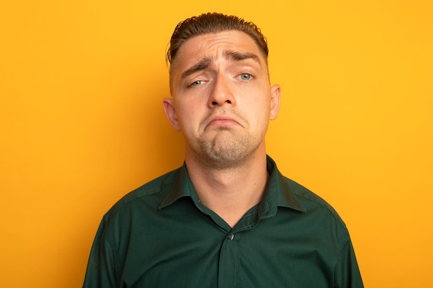 Infeliz joven guapo en camisa verde con expresión triste