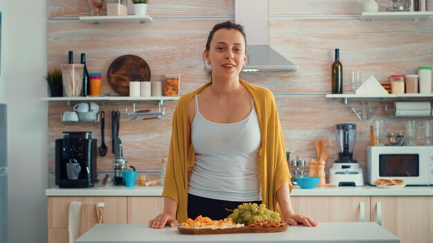 Foto gratuita influencer de vlogger mujer emplazamiento en la cocina de casa y hablando mirando a la cámara. influencer hablando hacer video chat, conferencia de grabación de estilo de vida vlog, vista de cámara web