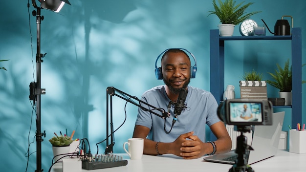 Influenciador afroamericano filmando video con cámara para canal vlog en estudio. Grabación de vlogger negro con micrófono, auriculares y tecnología para la carrera de las redes sociales en Internet