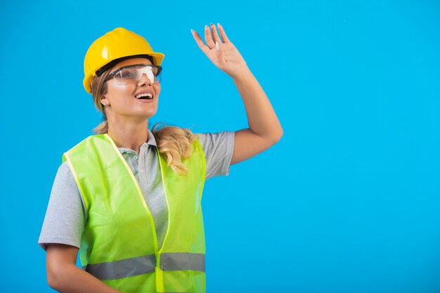 Ingeniera en casco amarillo y equipo con anteojos preventivos y mirando hacia arriba.