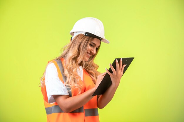 Ingeniera en casco blanco y equipo sosteniendo la lista de verificación y tomando notas.