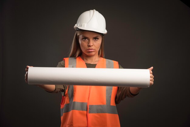 Ingeniera con un casco blanco que ofrece el plan del proyecto y parece motivada.