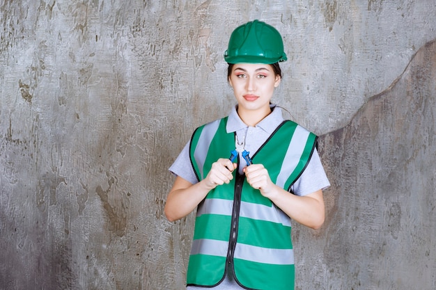 Ingeniera en casco verde sosteniendo alicates para un trabajo de reparación