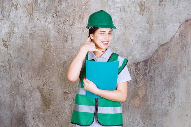 Ingeniera en casco verde sosteniendo una carpeta azul