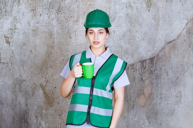 Ingeniera en casco verde sosteniendo una taza de café verde