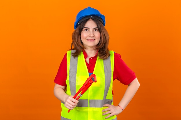 Foto gratuita ingeniera con chaleco de construcción y casco de seguridad con sonrisa en la cara con llave ajustable en mano sobre pared naranja aislada