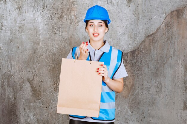 Ingeniera en uniforme azul y casco sosteniendo una bolsa de compras.