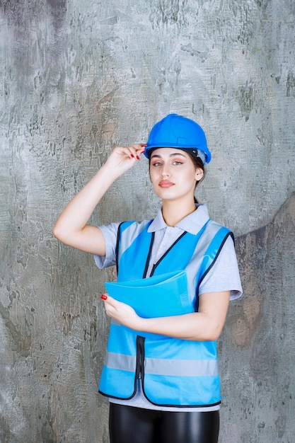 Ingeniera en uniforme azul y casco sosteniendo una carpeta de informe azul