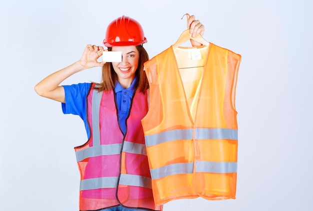 Foto gratuita ingeniera en uniforme presentando un pedazo de chaqueta de seguridad al colega y presentando su tarjeta de presentación.