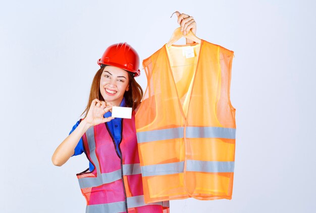 Ingeniera en uniforme presentando un pedazo de chaqueta de seguridad al colega y presentando su tarjeta de presentación.