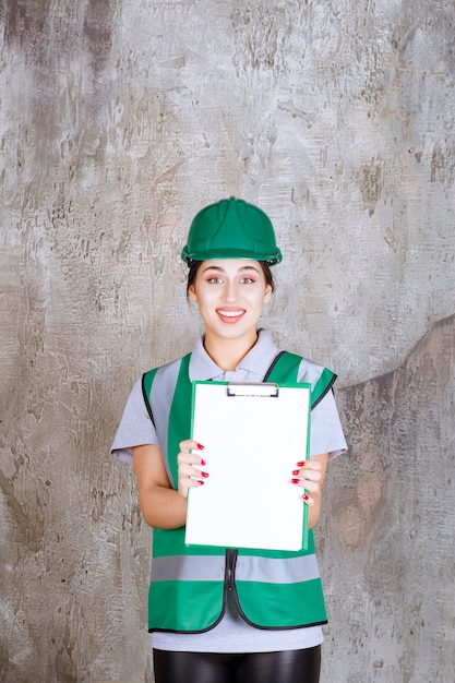 Ingeniera en uniforme verde y casco demostrando la hoja del proyecto