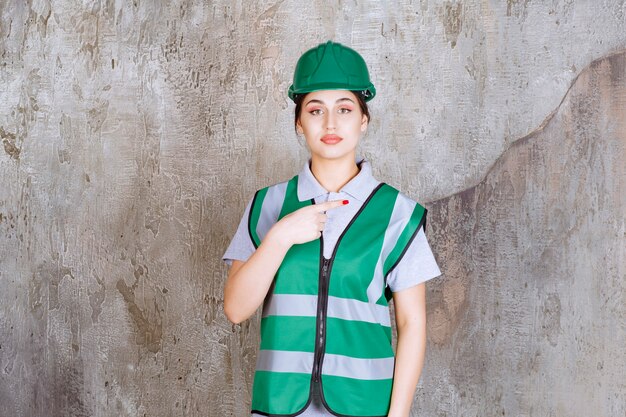 Ingeniera en uniforme verde y casco mostrando el lado derecho.