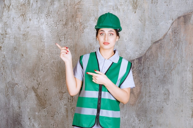 Ingeniera en uniforme verde y casco mostrando el lado izquierdo con emociones.