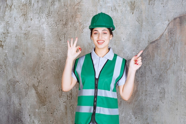 Ingeniera en uniforme verde y casco mostrando signo de mano positivo