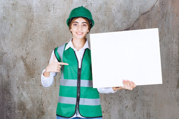 Foto gratuita ingeniera en uniforme verde y casco sosteniendo un tablero de información rectangular.