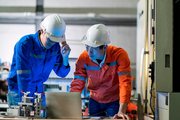 Ingeniero asiático masculino profesional que tiene una discusión de pie sobre la máquina cnc en la fábrica dos compañeros de trabajo asiáticos explican y resuelven el proceso de la máquina de operación cnc