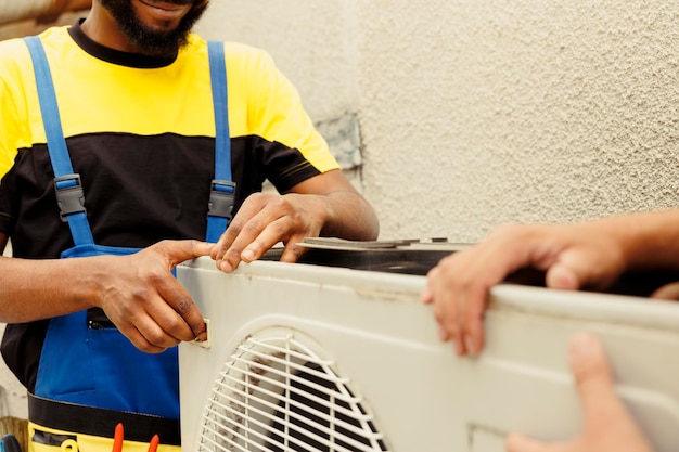 Un ingeniero capacitado y un técnico certificado abren un viejo sistema de climatización defectuoso para reemplazarlo con un nuevo aire acondicionado exterior de alto rendimiento después de drenar el refrigerante y reemplazar los conductos.