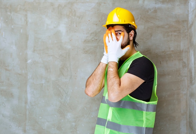 Ingeniero en casco amarillo y guantes industriales mirando a través de sus dedos