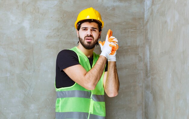 Ingeniero en casco amarillo y guantes industriales mostrando signo de pistola en la mano
