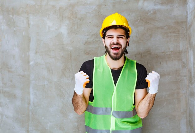 Ingeniero en casco amarillo y guantes industriales mostrando signo de satisfacción