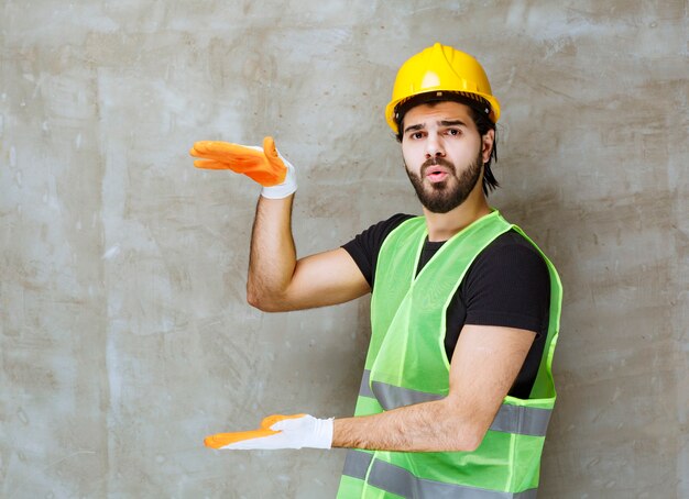 Ingeniero con casco amarillo y guantes industriales que muestran la altura de un objeto