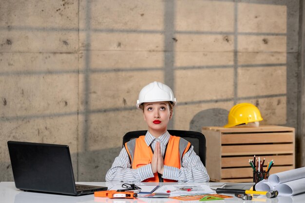 Ingeniero en casco y chaleco trabajador civil inteligente joven linda chica rubia rezando