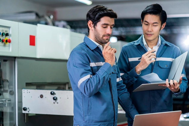 Ingeniero caucásico asiático masculino profesional que tiene una discusión de consulta permanente en la máquina en la fábrica dos compañeros de trabajo expertos explican y resuelven el proceso de la máquina de operación cnc